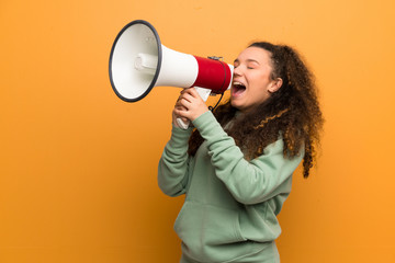 Teenager girl over ocher wall shouting through a megaphone