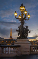 Fototapeta premium Paris, France - 03 17 2019: Quays of the Seine. View of Eiffel Tower from Alexander III Bridge by sunset