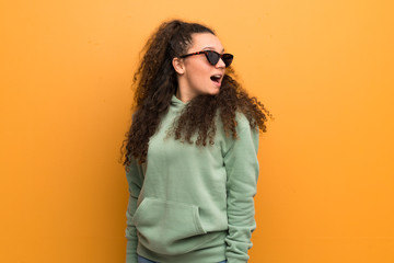 Teenager girl over ocher wall with glasses and smiling