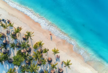 Fotobehang Luchtfoto van parasols, palmen op het zandstrand, mensen, blauwe zee met golven bij zonsondergang. Zomervakantie in Zanzibar, Afrika. Tropisch landschap met palmbomen, parasols, wit zand, oceaan. Bovenaanzicht © den-belitsky