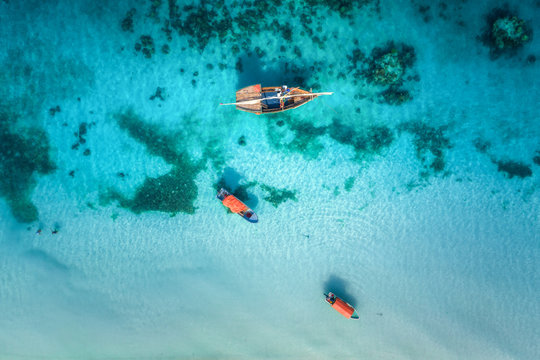 Aerial view of the fishing boats in clear blue water at sunny day in summer. Top view from drone of boat, sandy beach. Indian ocean in Zanzibar, Africa. Landscape with sailboats, clear sea. Seascape © den-belitsky