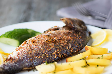 Baked dorada with potatoes on a white plate.