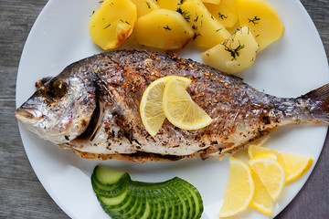 Baked dorada with potatoes on a white plate.