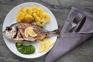Baked dorada with potatoes on a white plate.