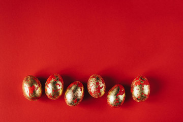 Six golden colored and decorated with sparkles Easter eggs on red background. Happy Easter greeting card. Copy space. Easter background.