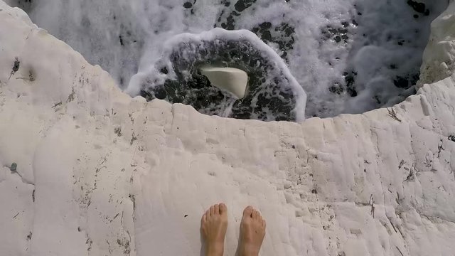 Women bare feet on white rock on famous Governors black sand beach, landmark of Cyprus. POV, slow motion.