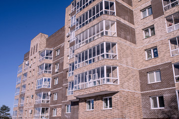 Fototapeta premium The new nine-storey house, illuminated by sunlight, is depicted in a sharp angle from the level of human growth against a clear sky, toned.