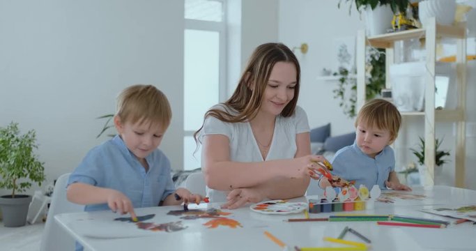 The family has fun painting on paper with their fingers in paint. Mom and two children paint with fingers on paper