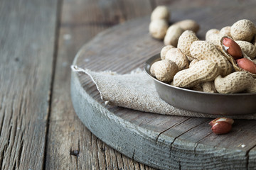 Peanuts in the shell and peeled close up in a cup. Background with peanuts. Roasted peanuts in the shell and peeled on a background of brown cloth in cups