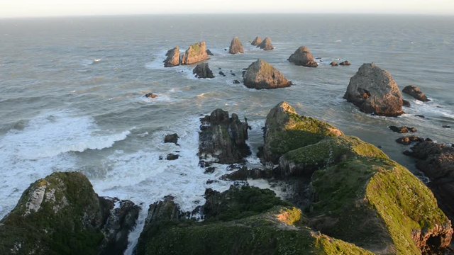 The setting sun illuminates boulders and waves of Nugget Point