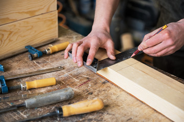 The worker makes measurements of a wooden board with ruler.