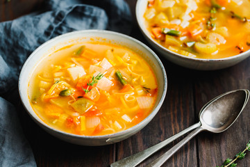 Spring vegetable soup with chicken stock for one person on wooden table.  Rustic style, close-up view.