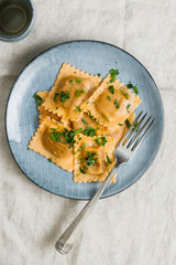 View from above on homemade Italian ravioli pasta with parsley on a blue ceramic plate.