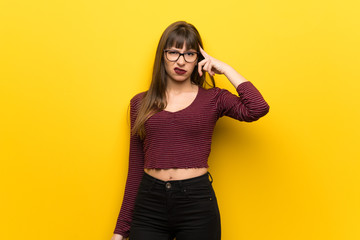 Woman with glasses over yellow wall making the gesture of madness putting finger on the head