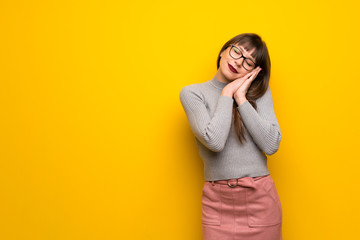 Woman with glasses over yellow wall making sleep gesture in dorable expression