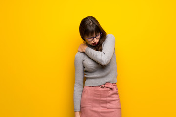 Woman with glasses over yellow wall suffering from pain in shoulder for having made an effort