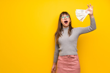 Woman with glasses over yellow wall taking a lot of money
