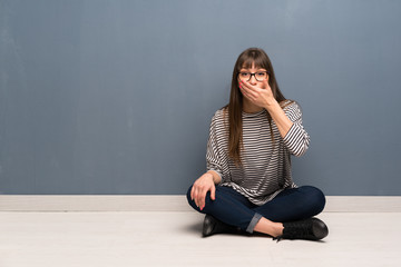 Woman with glasses sitting on the floor covering mouth with hands for saying something inappropriate