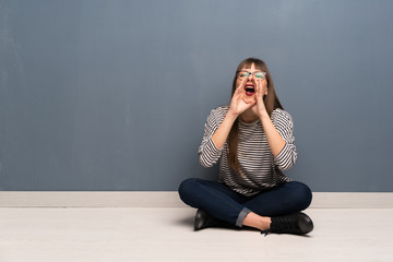 Woman with glasses sitting on the floor shouting and announcing something