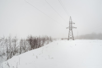 between the wooden supports stretched electrical wires. winter landscape and fog