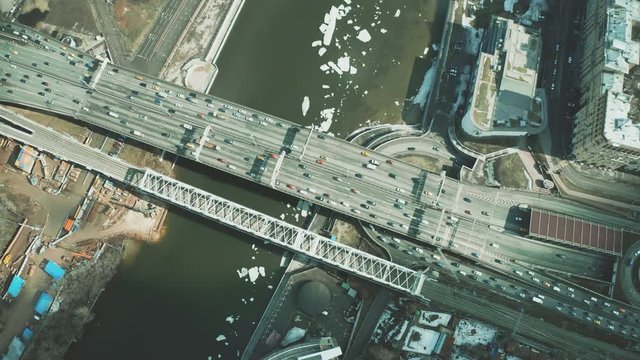 Aerial down view of cars moving along the bridge across icy river