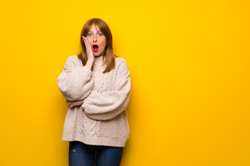 Redhead woman over yellow wall surprised and shocked while looking right