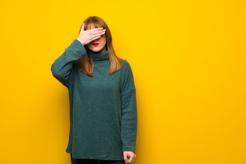 Woman with glasses over yellow wall covering eyes by hands. Do not want to see something