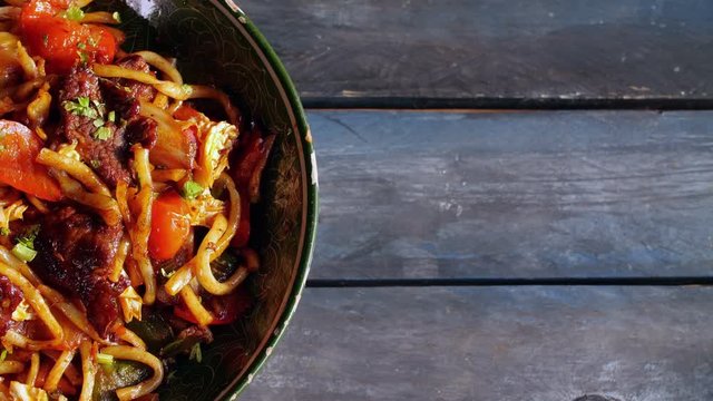 Traditional lagman with vegetables and meat. Rotates on a wooden background. Top view with the copy space for your text.
