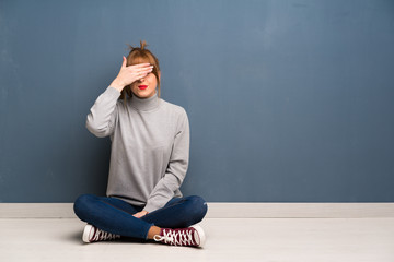 Redhead woman siting on the floor covering eyes by hands. Do not want to see something