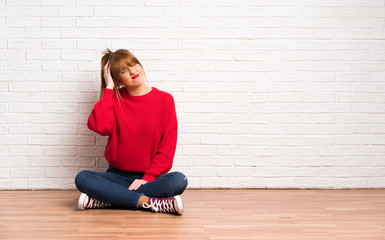 Redhead woman siting on the floor with an expression of frustration and not understanding