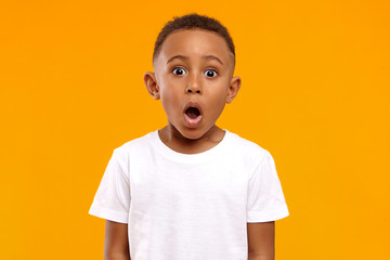 Fototapeta Surprise, excitement and fascination concept. Funny bug eyed African little boy opening his mouth widely, shocked with astonishing unexpected news, having amazed look, showing full disbelief obraz