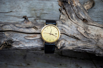 gold wrist watch with leather strap on wooden background