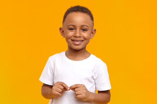 People, childhood, school age and lifestyle concept. Horizontal studio image of handsome adorable African American schoolboy dressed in white t-shirt, looking at camera with broad happy smile