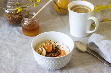 Breakfast of granola with yogurt and tea and forsythia flowers on a linen tablecloth. Rustic style.