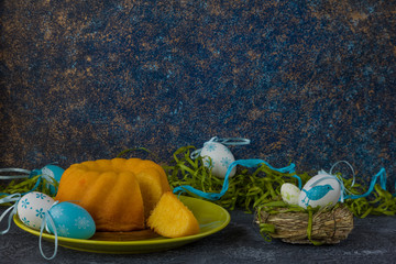 Easter bread on green plate and painted Easter eggs ion dark stone table decorated with green grass