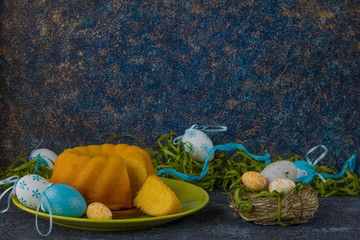Easter bread on green plate and painted Easter eggs ion dark stone table decorated with green grass