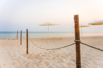 Rope fence on the sandy beach, white beach umbrellas. Sunset on the beach.