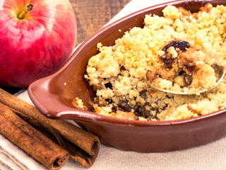 Homemade apple cramble cake with fresh apples and cinnamon sticks on rustic dark wooden background