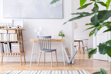 Stylish scandinavian home decor of interior with creative wooden desk, bamboo bookstand with accessories, books and plants. Open space and living room. Brown wooden parquet and stylish carpet. © FollowTheFlow