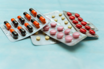 Multicolored pills and capsules in blisters close-up, on blue background. The concept of treating human diseases.
