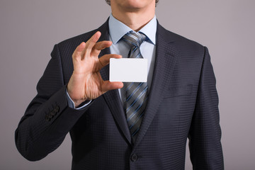 Hand of a businessman with a blank card on a gray background.