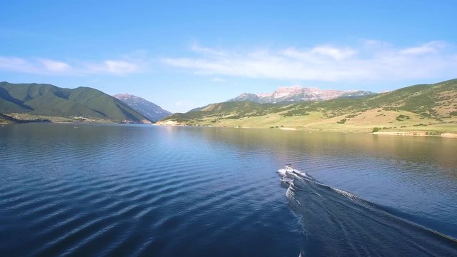 aerial shot of speed boat with water skier and green spring. A speed boat with a water skier travels across a calm mountain valley lake.