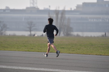 A young man is jogging on an airport runway.