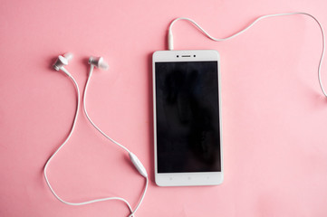 Close-up of a smartphone with headphones on a pink background. View from above. Listen to music