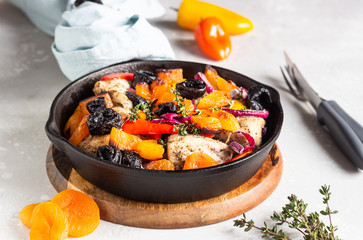 Grilled chicken with vegetables (bell pepper, carrot and onion) and dried fruits (apricots and prunes) in a cast-iron pan. Light gray background. Copy space. Healthy food.