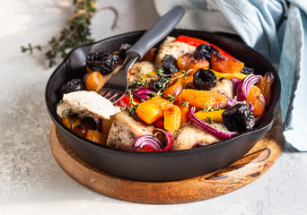 Grilled chicken with vegetables (bell pepper, carrot and onion) and dried fruits (apricots and prunes) in a cast-iron pan. Light gray background. Copy space. Healthy food.
