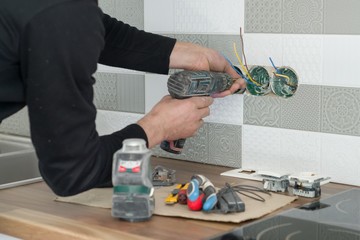 Renovation and construction in kitchen, close-up of electricians hand installing outlet on wall with ceramic tiles using professional tools