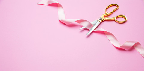 Grand opening. Gold scissors cutting pink satin ribbon, pink background