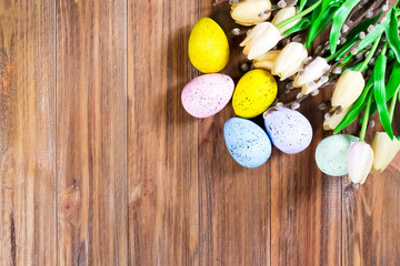 Multi-colored Easter eggs with tulips on a wooden brown background with space for text. Easter layout for your ideas. Flat lay