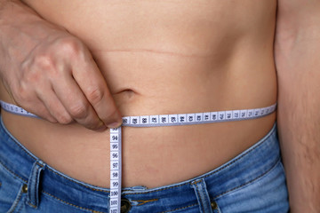 Diet concept, man with naked torso with measuring tape around the waist. Weight loss, slimming, health care